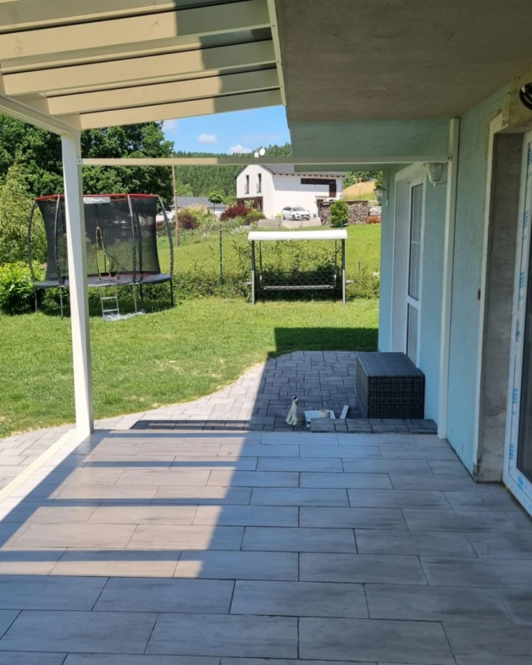 Vue depuis le dessous de la pergola en aluminium en cours de construction sur le jardin, avec un trampoline et une balançoire