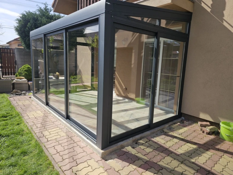 Une véranda moderne vitrée, dotée d'une structure en aluminium anthracite et de portes coulissantes, sur la terrasse d'une maison individuelle.