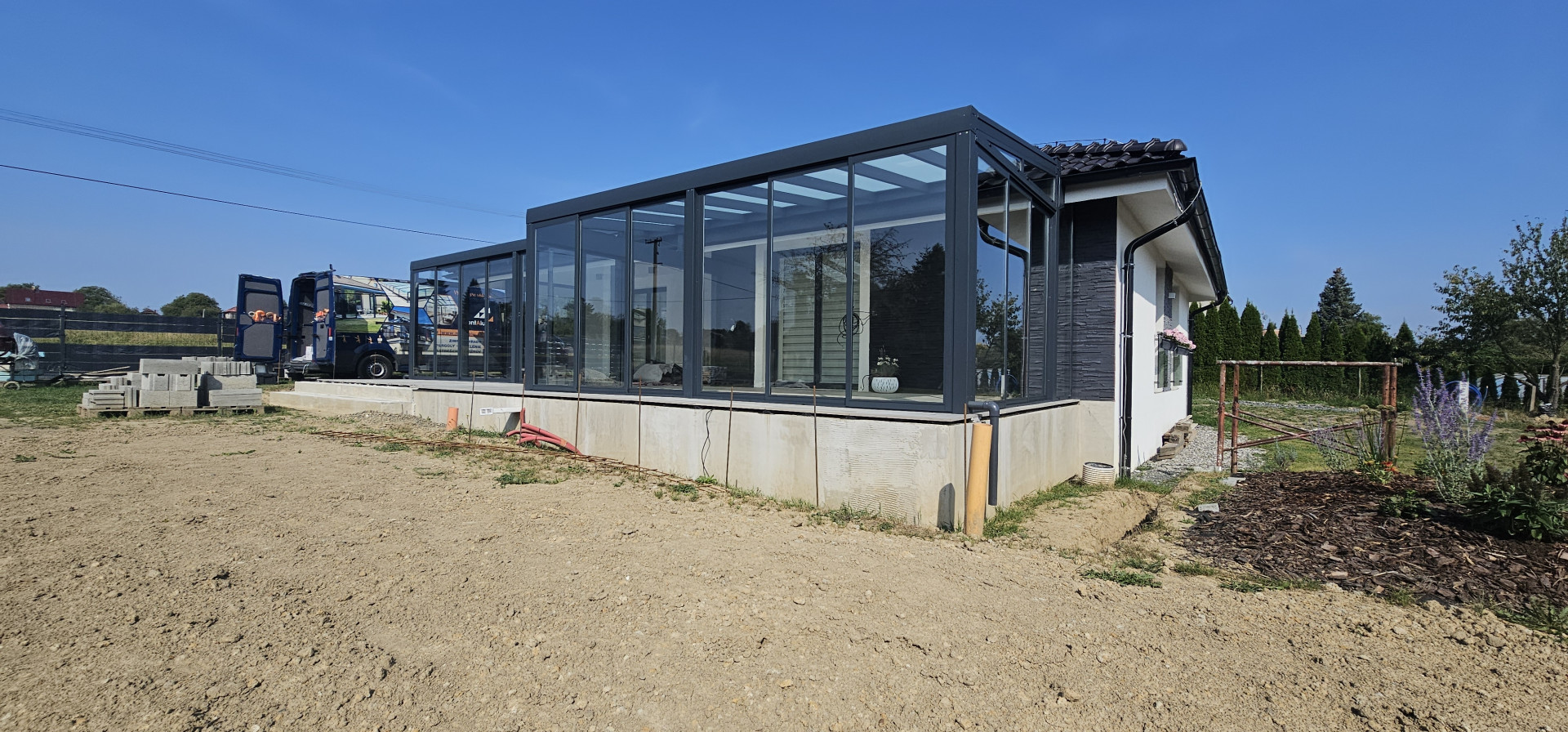 Une véranda moderne vitrée, dotée d'une structure anthracite, en cours de construction à Ostrava, attenante à une maison individuelle.
