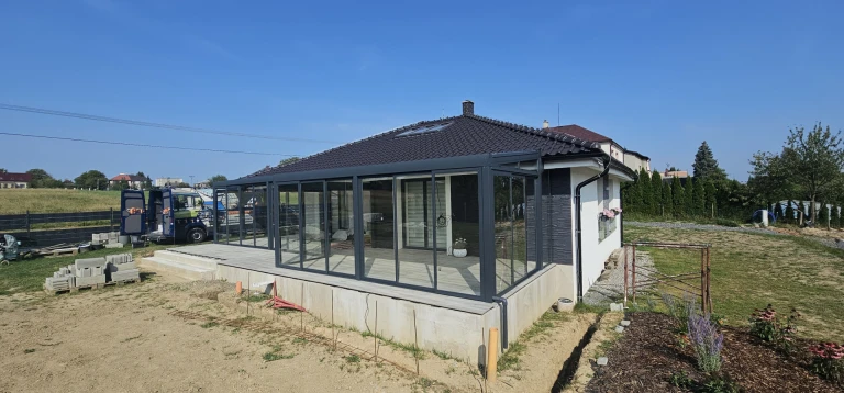Une véranda moderne vitrée, dotée d'une structure anthracite, construite à côté d'une maison individuelle