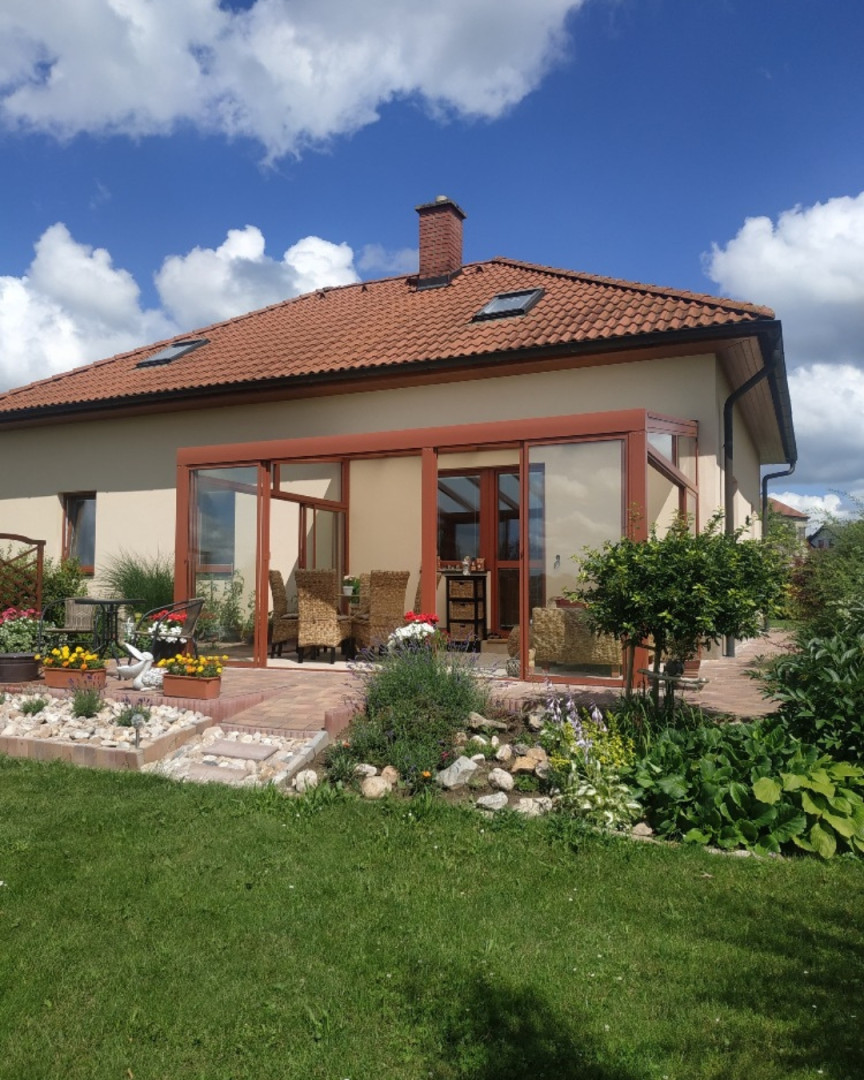 Une véranda moderne vitrée, dotée d'une structure marron, attenante à une maison individuelle avec un jardin aménagé.