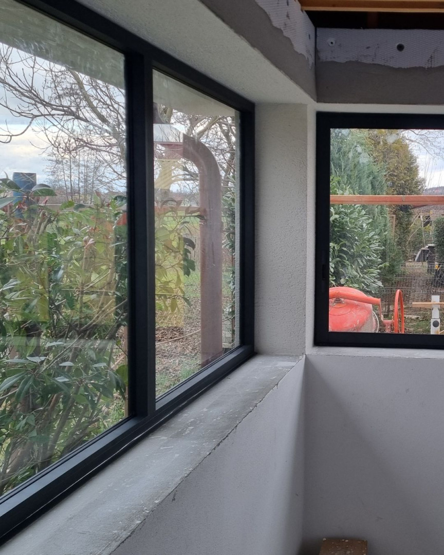 Vue détaillée de la baie vitrée d'angle de la terrasse, avec ses cadres en aluminium foncé et sa vue sur le jardin.