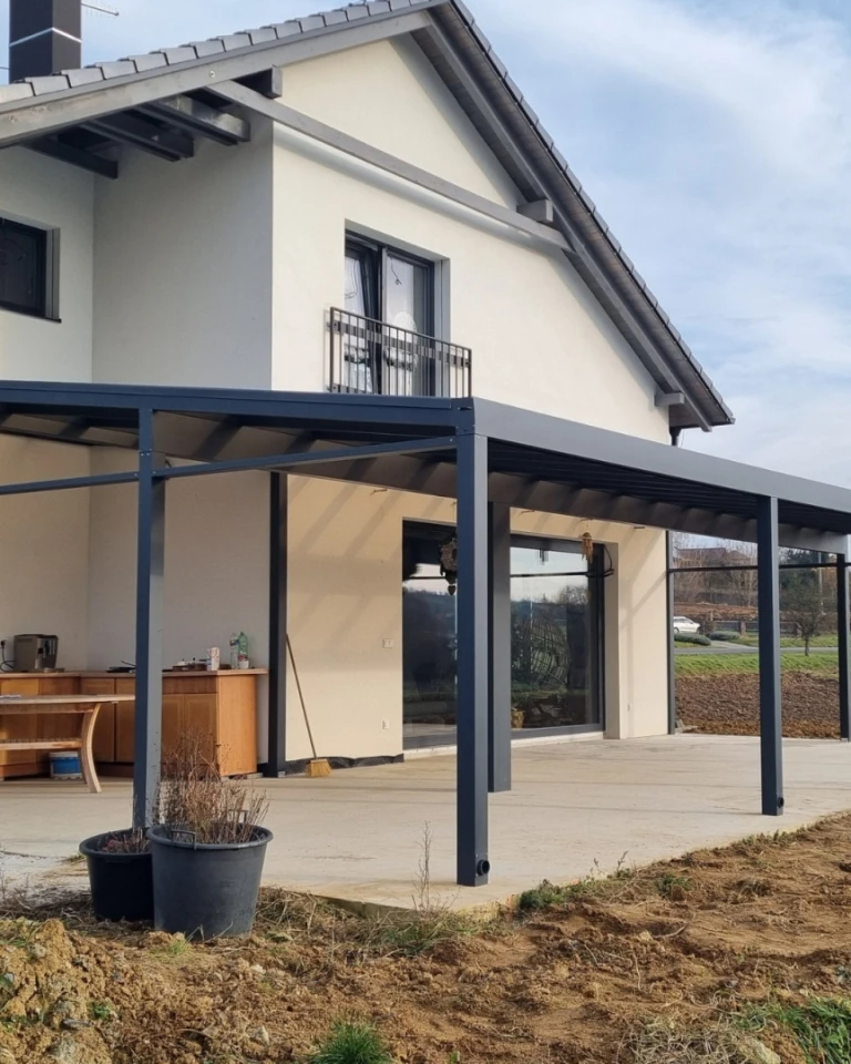 Une pergola moderne en aluminium, avec une structure gris foncé, installée près d'une maison individuelle