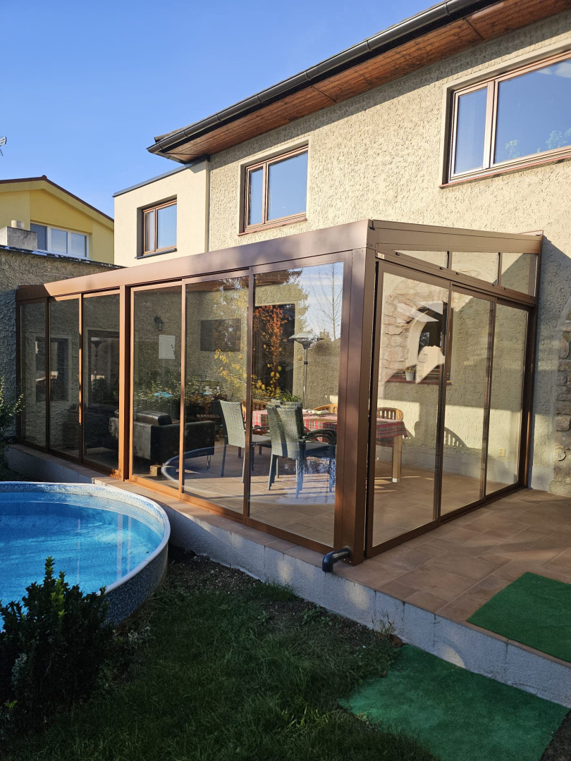 Une véranda moderne vitrée, dotée d'une structure marron, attenante à une maison individuelle avec piscine