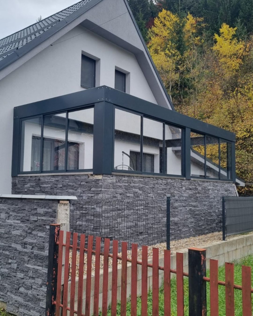 Vitrage moderne de la terrasse d'une maison individuelle, avec un cadre foncé et un revêtement en pierre