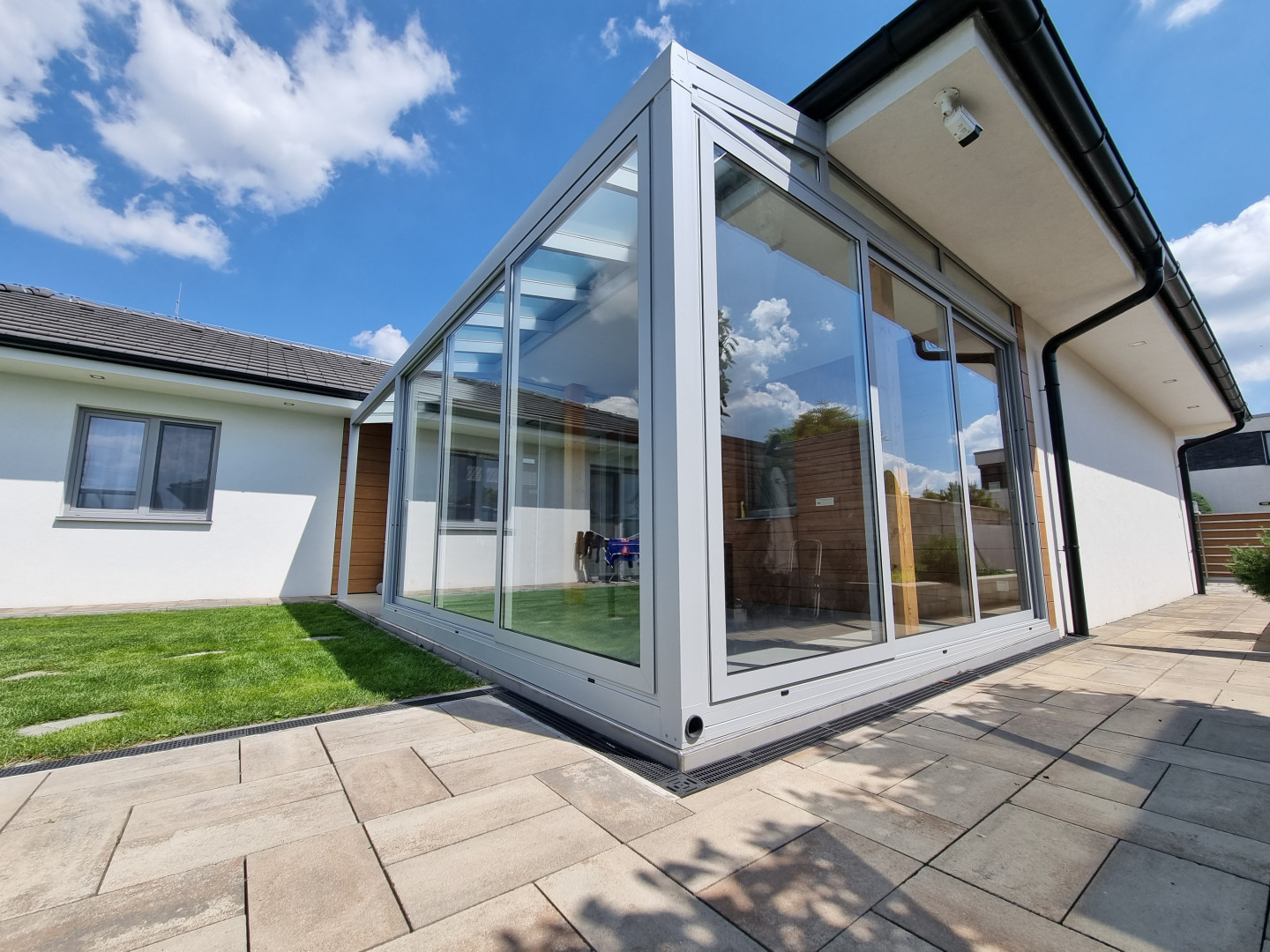 Une véranda moderne vitrée, dotée d'une structure en aluminium, attenante à une maison individuelle et donnant sur la pelouse