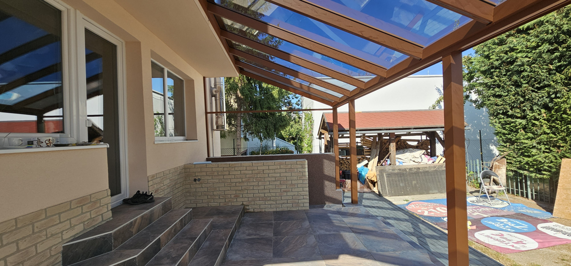 Pergola en aluminium imitation bois avec toiture en verre, installée sur la terrasse d'une maison individuelle.