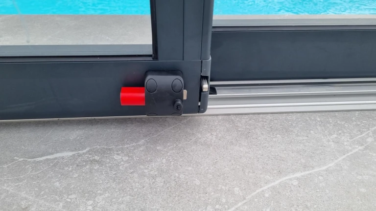 Détail du mécanisme de verrouillage d'un abri de piscine en aluminium avec loquet rouge
