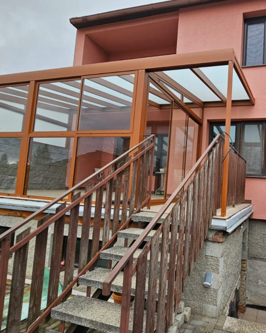 Pergola en aluminium vitrée de couleur marron installée sur la terrasse d'une maison dotée d'un escalier