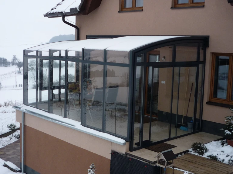 Une véranda moderne coulissante aux parois vitrées, recouverte de neige, sur la terrasse d'une maison individuelle en hiver.
