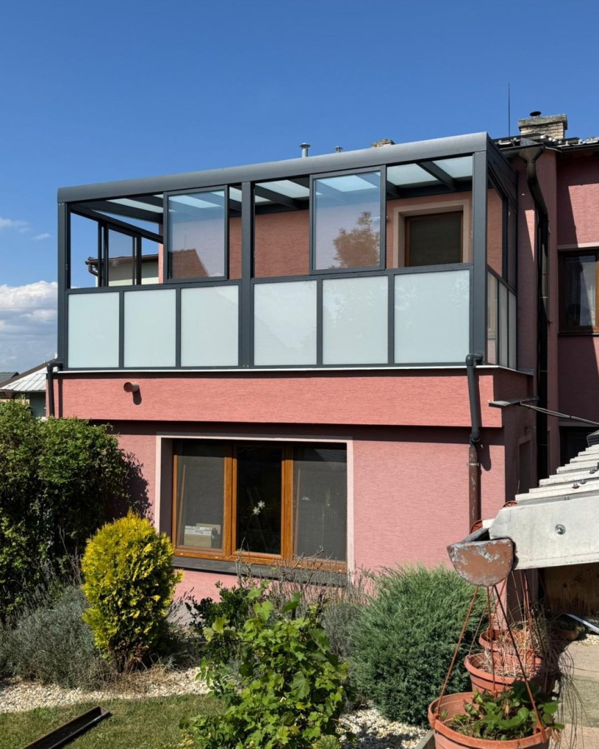 Une pergola moderne vitrée, dotée d'un cadre en aluminium gris foncé et de vitres laitées, installée sur le balcon d'une maison individuelle.