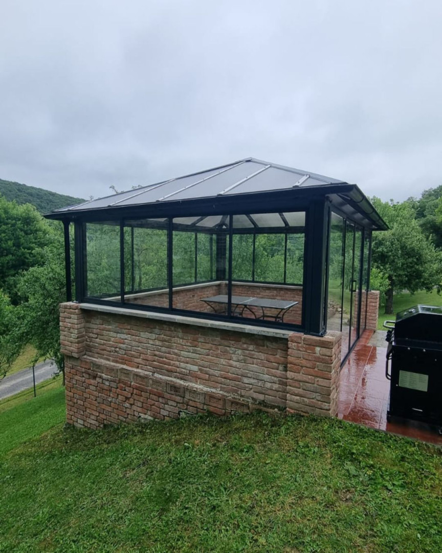 Une tonnelle moderne vitrée avec une base en briques dans le jardin