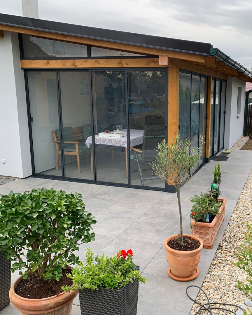 Vitrage moderne de la terrasse avec un système coulissant et une structure en bois, près d'une maison individuelle, avec des jardinières au premier plan.