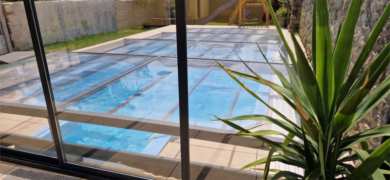 Une couverture de piscine moderne et basse, dotée de panneaux translucides, dans le jardin