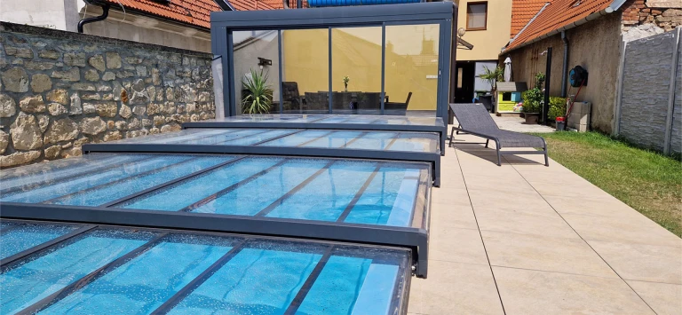 Une couverture de piscine télescopique moderne et basse, dotée d'un cadre en aluminium anthracite, installée sur la terrasse près de la maison.