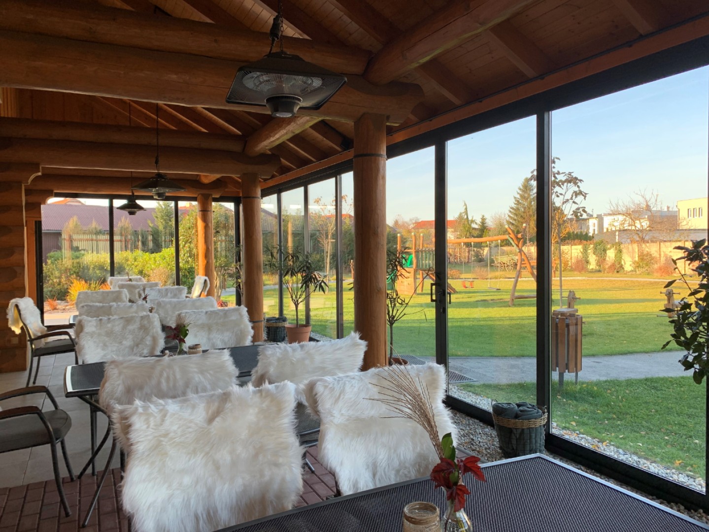 Terrasse vitrée d'une maison en rondins avec vue sur le jardin et l'aire de jeux pour enfants