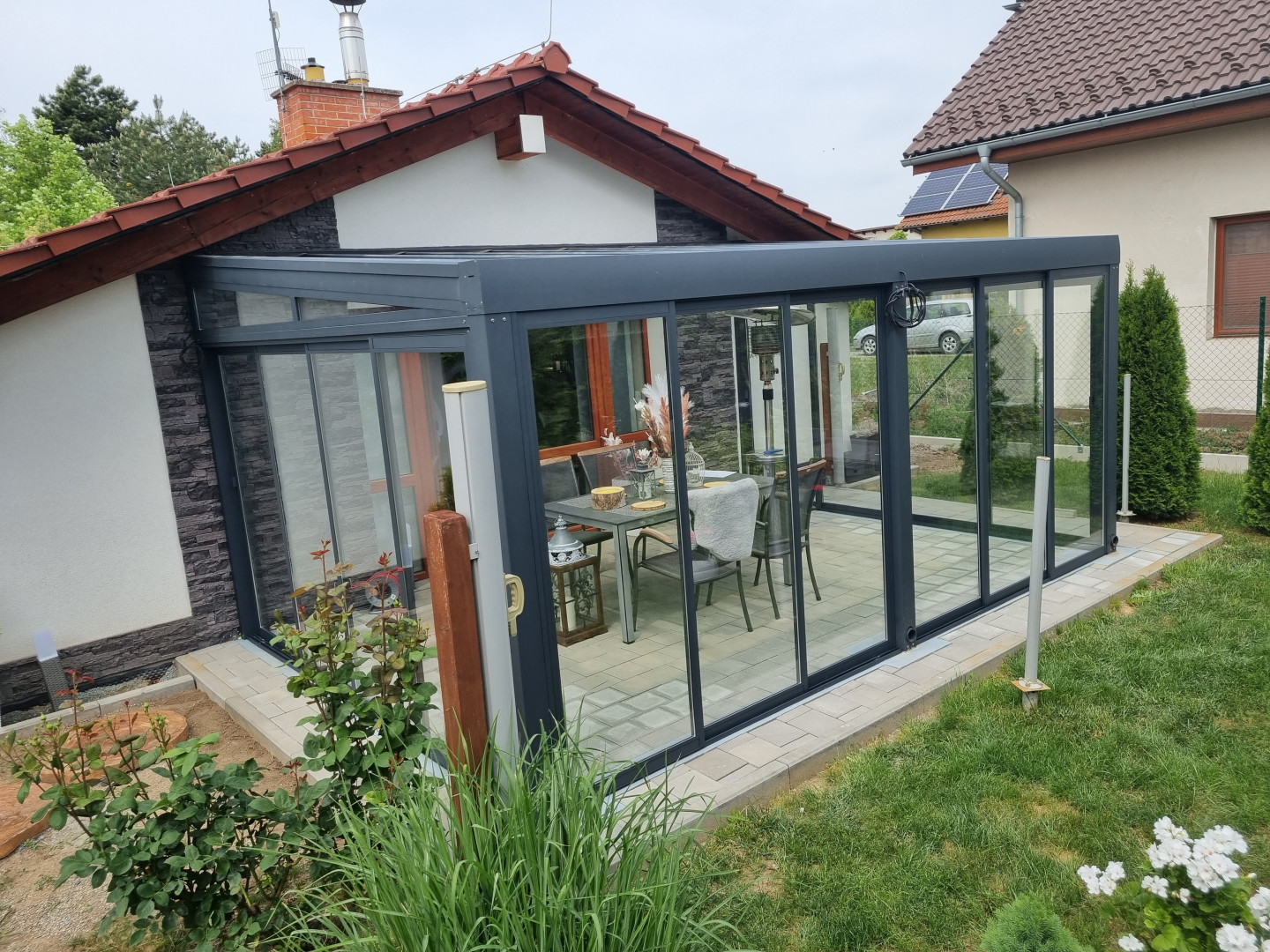 Une véranda moderne vitrée, dotée d'une structure anthracite et de portes coulissantes, attenante à une maison individuelle