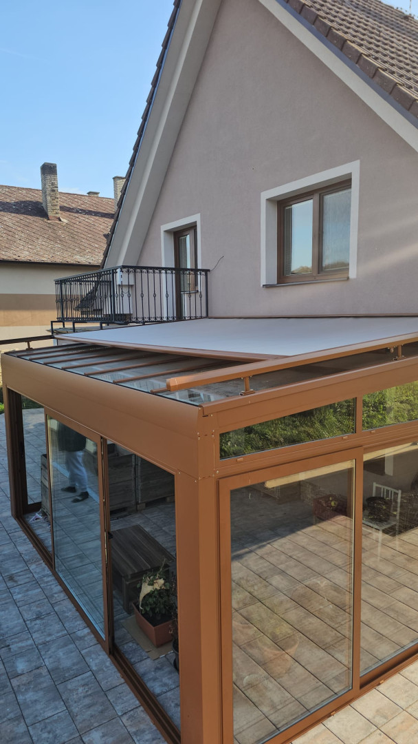 Une véranda vitrée avec une structure marron et un store coulissant sur la terrasse d'une maison individuelle