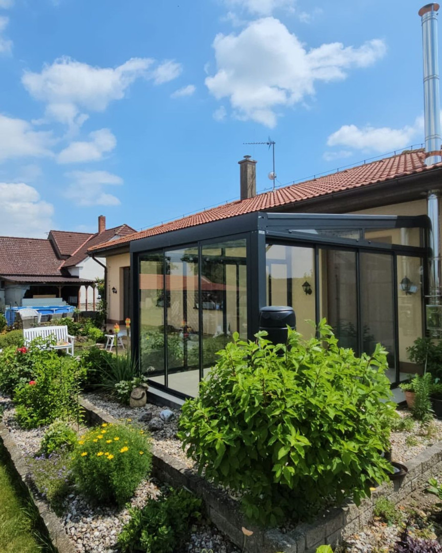 Une véranda moderne vitrée, dotée d'une structure anthracite, attenante à une maison individuelle avec un jardin bien entretenu