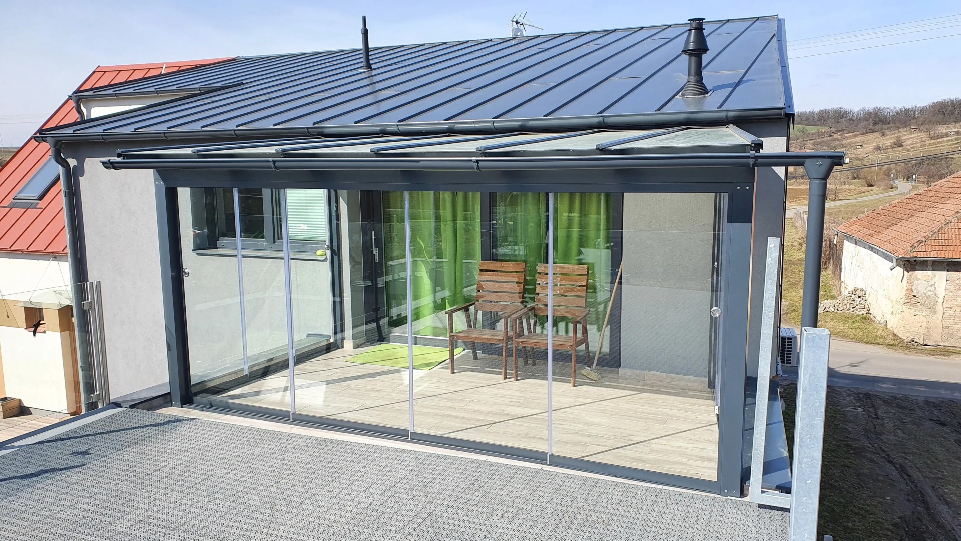 Une véranda moderne vitrée, dotée d'une structure anthracite et d'un vitrage coulissant, sur la terrasse de la maison.
