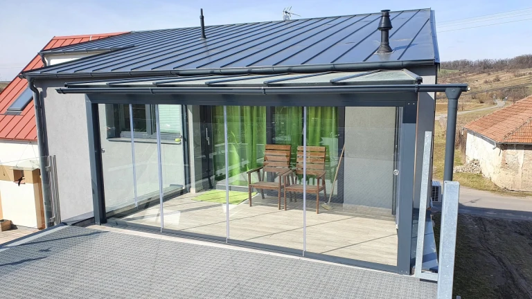 Une véranda moderne vitrée, dotée d'une structure anthracite et d'un vitrage coulissant, sur la terrasse de la maison.