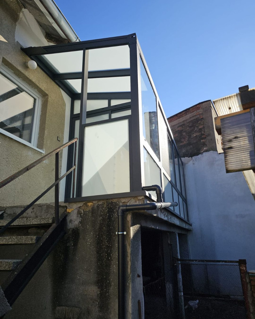 Structure vitrée moderne de la véranda « Robust », avec un cadre foncé, fixée au mur de la maison.